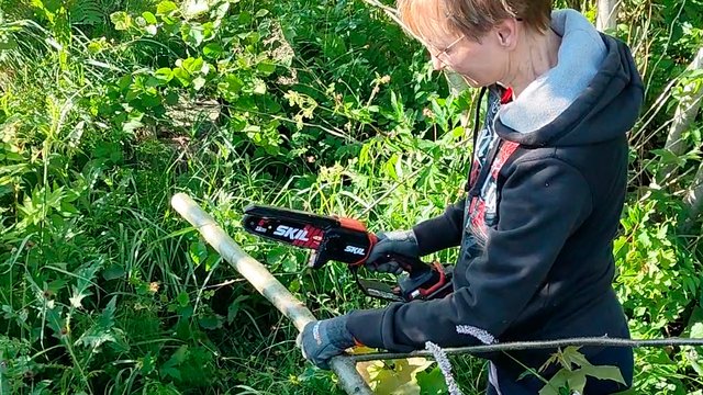 henkilö karsii ohuita puita akkuoksasahalla ojanpohjalla ryteikössä